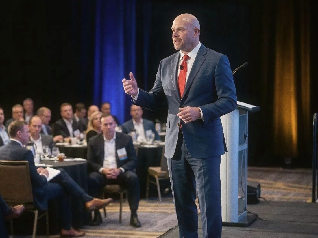 Dean Eric Smith speaking at a podium to a ballroom of executives seated at round tables